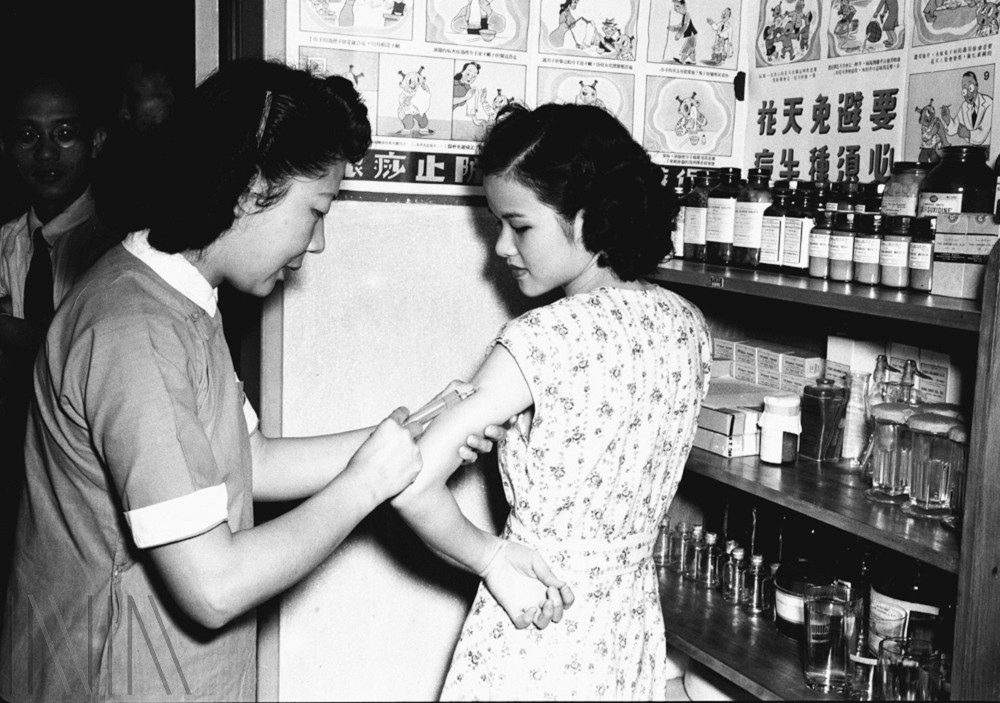 圖1 1950年代護理人員替民眾注射疫苗針劑，牆上還有「要避免天花必須種牛痘」的宣導海報